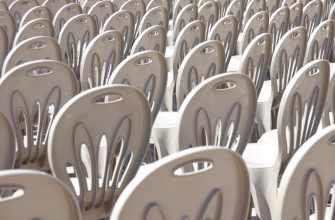 Rows of beige plastic chairs arranged in orderly rows, creating a dense, stadium-like seating pattern. Empty seats in a sunlit setting.