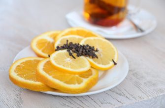 Plate of orange slices topped with chocolate shavings on a white plate; a glass of tea blurred in the background.