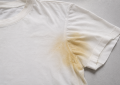 White T-shirt with a large yellow underarm stain on the sleeve area. A plain white tee showing a yellow stain along the upper sleeve near the armpit. White short-sleeve shirt featuring a noticeable yellow armpit stain on the sleeve. Plain white T-shirt with an evident yellow stain spreading from the underarm toward the sleeve. A white tee shirt laid flat with a prominent yellow discoloration on the sleeve near the armpit.