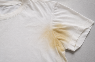 White T-shirt with a large yellow underarm stain on the sleeve area. A plain white tee showing a yellow stain along the upper sleeve near the armpit. White short-sleeve shirt featuring a noticeable yellow armpit stain on the sleeve. Plain white T-shirt with an evident yellow stain spreading from the underarm toward the sleeve. A white tee shirt laid flat with a prominent yellow discoloration on the sleeve near the armpit.