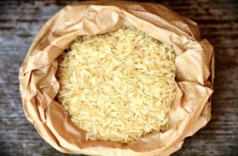 Uncooked white rice in an open brown paper bag on a wooden surface.