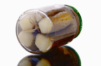 Glass jar of pickled garlic cloves in brine, lying on its side with a green lid on a white background.