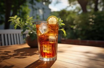 Tall glass of iced tea with ice cubes, a lemon slice, and mint on a sunlit wooden table in a garden.