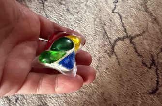 Hand holding a small clear blister-pack with five colorful gummy candies (red, yellow, green, blue) against a textured carpet background.