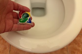 Rainbow-colored dental retainer held in a hand in front of a toilet bowl in a bathroom setting
