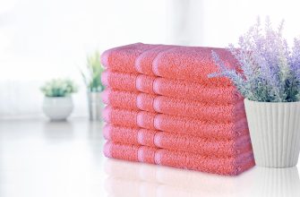 Stack of pink towels folded neatly beside a white pot with lavender flowers on a glossy surface.