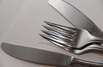 Close-up of a stainless steel fork and knives resting on a white surface, showing their reflective metal and blades touching the background edge.