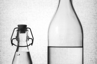 Two glass bottles with swing-top caps on a dark surface: a tall bottle beside a shorter one, both containing clear liquid.