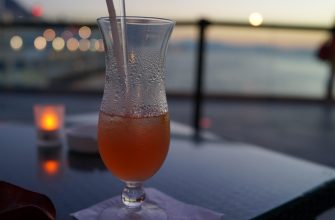 Frosted tropical cocktail in a tall hurricane glass with a straw on a seaside patio at sunset.