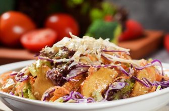 Crispy chicken and mixed greens salad with purple cabbage and sesame seeds in a white bowl, close-up.