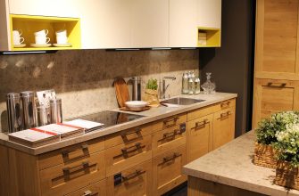 Modern kitchen showroom with wooden cabinets, grey countertop, and a sink area under white cabinets with yellow open shelves above.