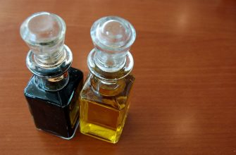 Two square glass bottles with glass stoppers, one dark liquid and one amber oil, on a wooden table surface.