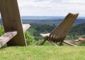 Wooden outdoor lounge chair on a grassy hill overlooking a valley of fields and forests.