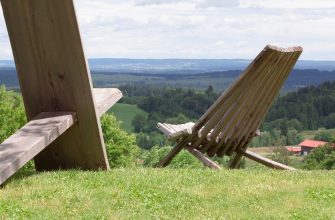 Wooden outdoor lounge chair on a grassy hill overlooking a valley of fields and forests.