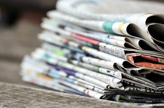 Pile of folded newspapers stacked on a wooden surface, ready for delivery or reading.