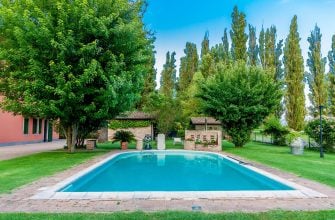 Rectangular outdoor pool with brick coping, surrounded by green lawn and tall trees under a bright blue sky.