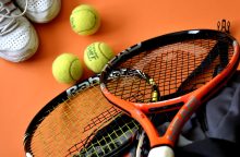 Tennis gear on an orange surface: three yellow tennis balls, an orange racket, and white sneakers in the corner.