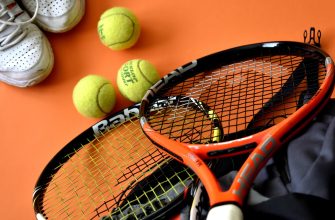 Tennis gear on an orange surface: three yellow tennis balls, an orange racket, and white sneakers in the corner.