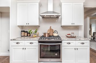 Modern white kitchen centered on a stainless steel stove with a range hood, white cabinets and a light subway tile backsplash.