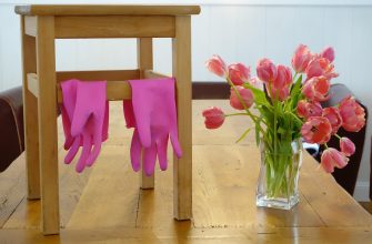 Pink rubber gloves draped over the rung of a wooden chair on a dining table, beside a vase of pink tulips.