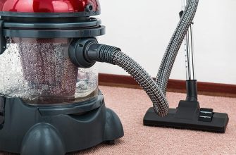 Canister vacuum with a flexible hose attached, cleaning a pink carpet in a home setting
