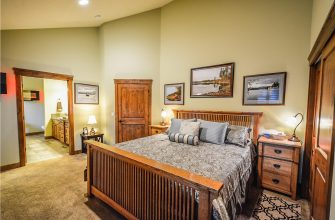 Warm master bedroom with a wooden bed, matching nightstands, and green walls; framed landscape art above the headboard.